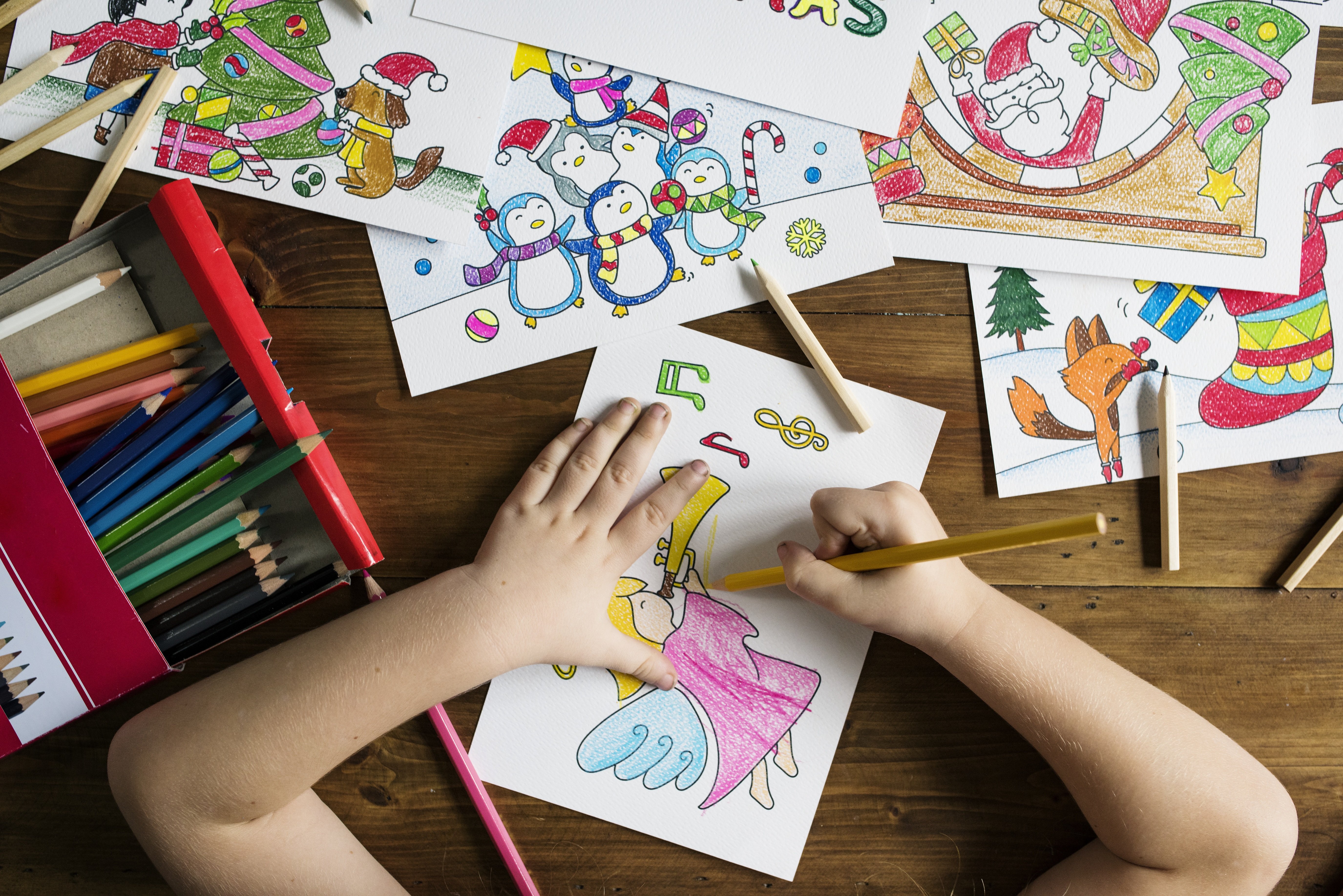 Criança colorindo desenho de anjo com lápis de cor em mesa com ilustrações de Natal